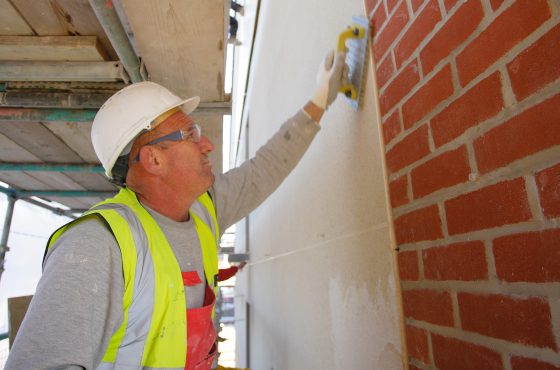 Construction worker on scaffolding applying render finish to block work on building exterior