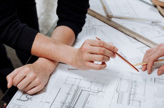 Hands holding pen over unravelled architectural drawings on table