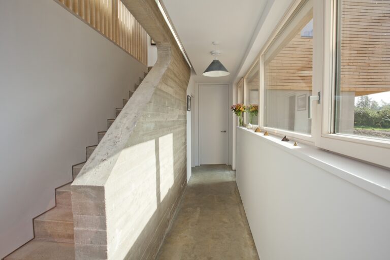 Corridor of residential project with plaster finish to walls and shadow gap detailing up length of stairs