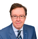 Portrait photo of man with navy suit jacket, light blue shirt, tie and glasses on white background