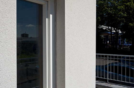 Scraped render finish to building exterior and around window reveal, railing to side of building