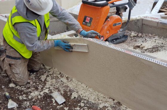 Construction worked on knees smoothing finish to render top coat applied on top of PVCu beading