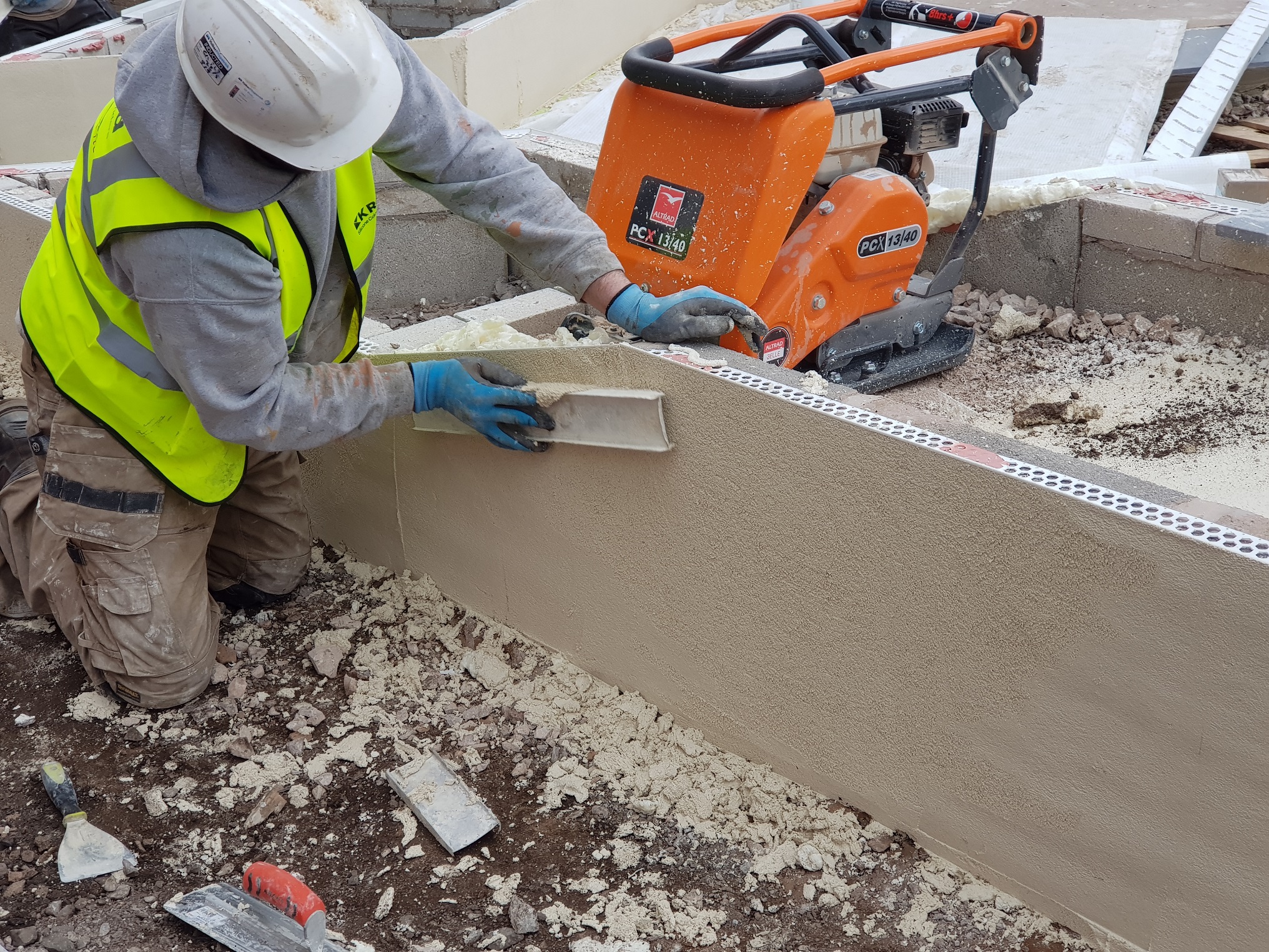 Construction worked on knees smoothing finish to render top coat applied on top of PVCu beading