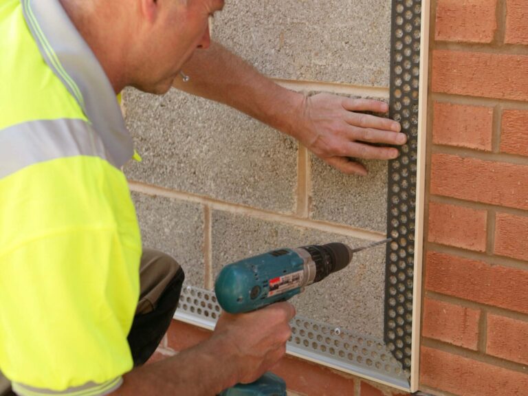 Mix of red brick and breeze block finish, with construction worker drilling into breeze block to fix render stop bead to wall