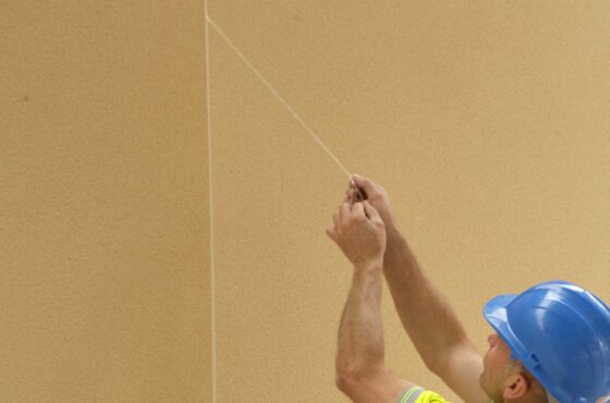 Construction worker with hard hat on on removing protective strip to front of expansion joint bead before render sets