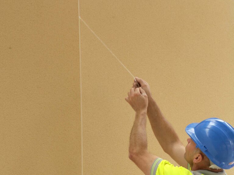 Construction worker with hard hat on on removing protective strip to front of expansion joint bead before render sets