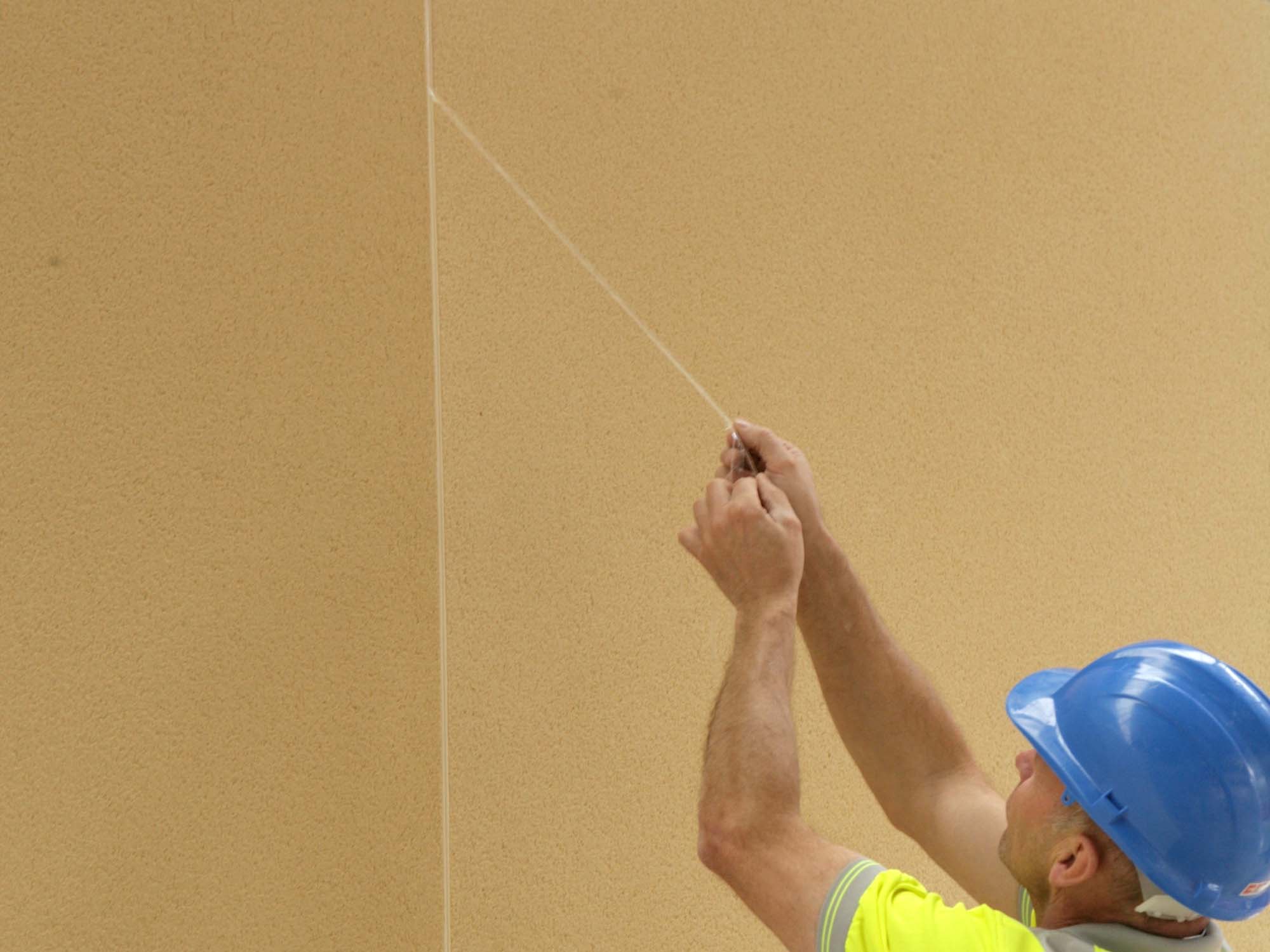 Construction worker with hard hat on on removing protective strip to front of expansion joint bead before render sets