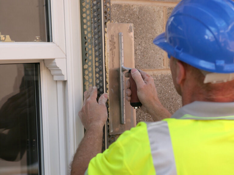 Construction worker applying render dabs the wings of PVCu render beading to attach it directly to breeze blocks at window reveal on building exterior