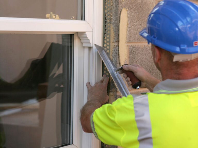 Construction worker applying render dabs to set stop PVCu beading to window reveals