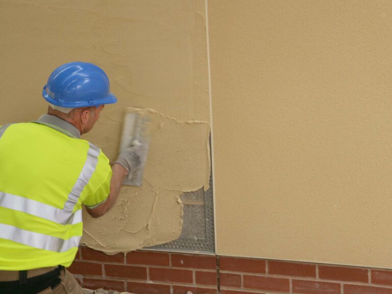 Construction worker with high vis top and blue hard hat applying render finish to external wall