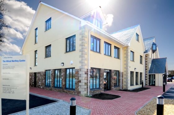 Signage for building to foreground with red brick path leading to rendered building