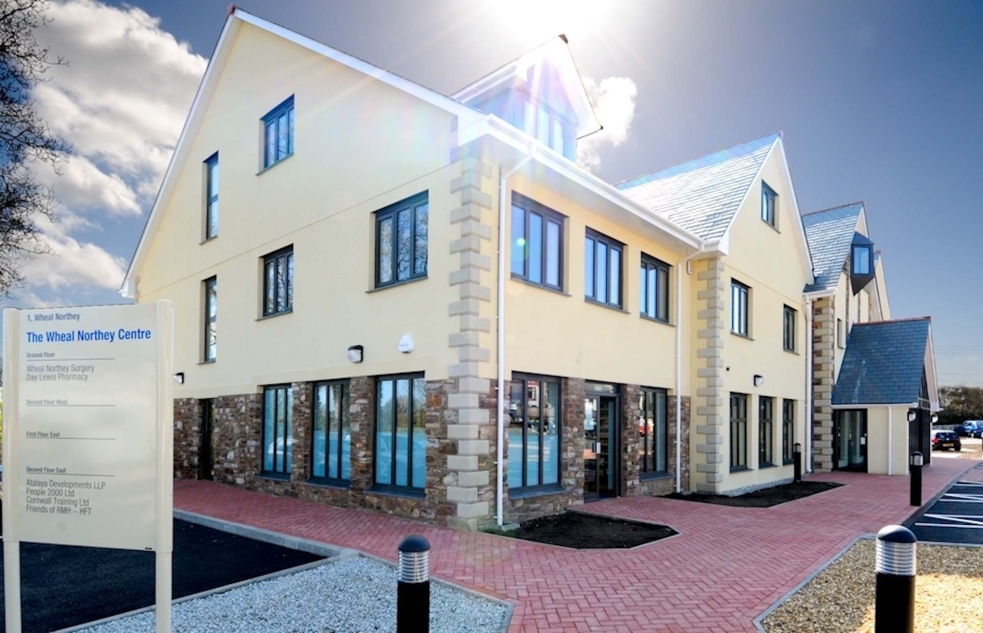 Signage for building to foreground with red brick path leading to rendered building