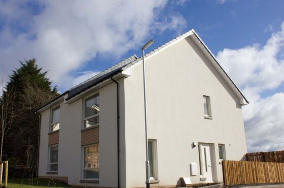 White rendered house with 4 windows to front and door to right hand face of building, fence running along right hand side